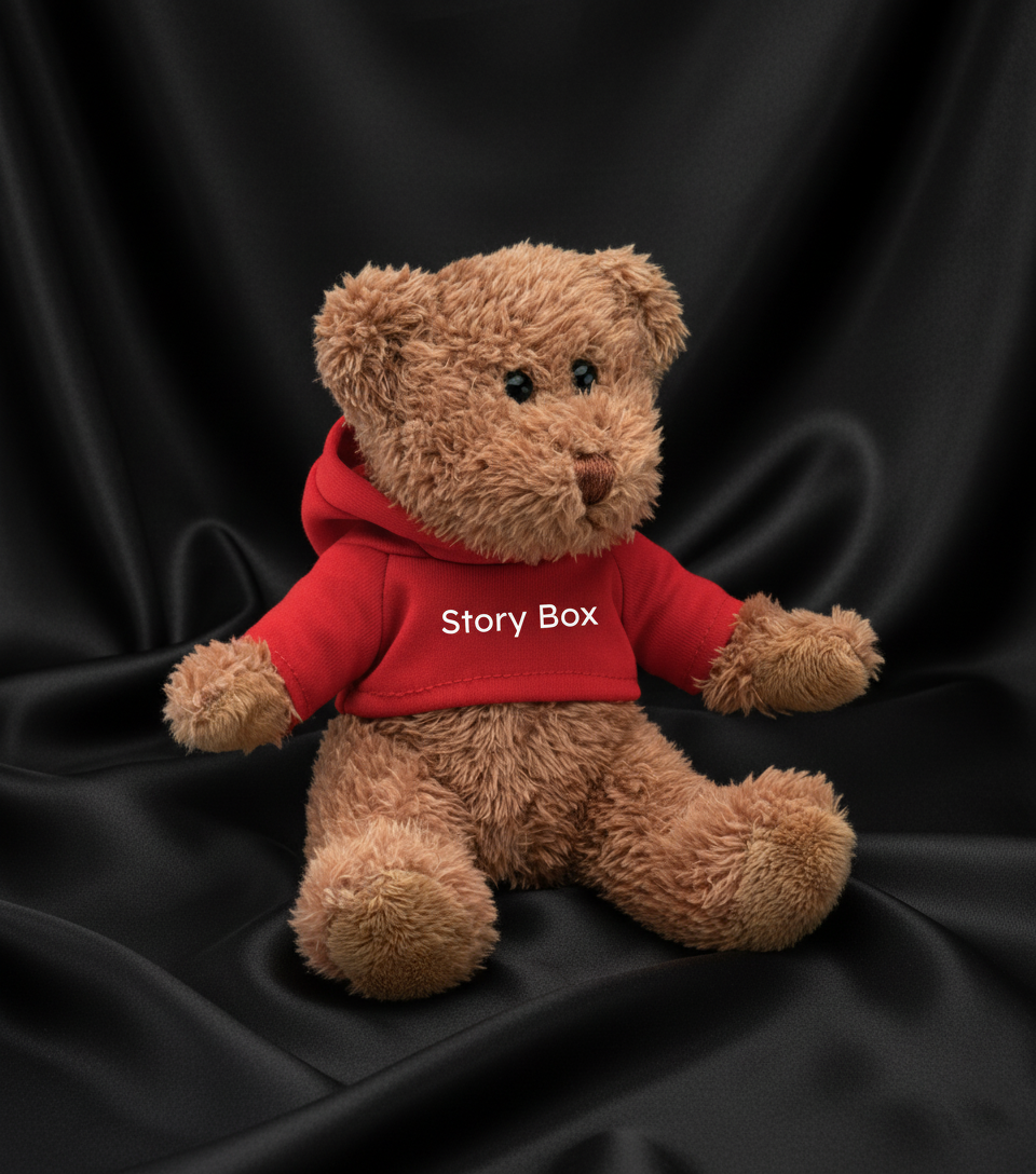 Ursuleț de pluș bej îmbrăcat cu hanorac roșu StoryBox, fotografiat pe fundal negru satinat, accesoriu din seturile cadou StoryBox.
